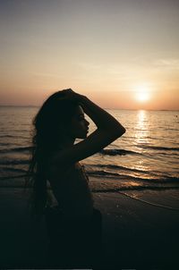 Silhouette woman standing at beach against sky during sunset