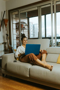 Woman using laptop while sitting on sofa