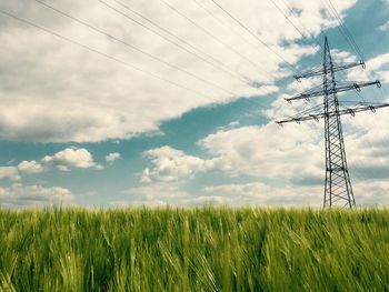 Electricity pylon on grassy field against sky