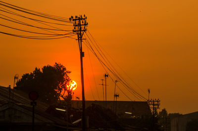 Low angle view of silhouette electricity pylon against orange sky