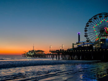 Ferris wheel at beach against clear sky during sunset