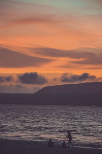 Silhouette people on beach against sky during sunset