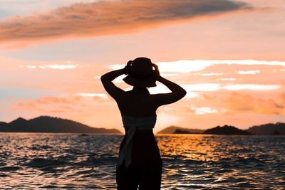 Silhouette woman standing by sea against sky during sunset