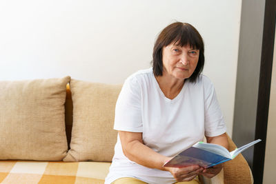 Young woman reading book while sitting on sofa at home