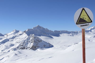 Warning sign by snow covered mountains against clear blue sky