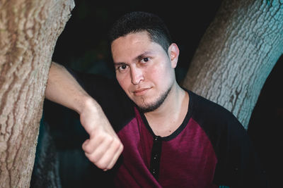 Portrait of young man by tree trunk at night