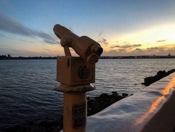 Coin-operated binoculars by sea against sky during sunset