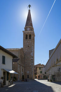 Low angle view of cross amidst buildings against clear blue sky