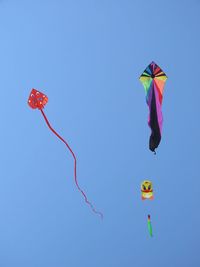 Low angle view of kites flying against clear blue sky