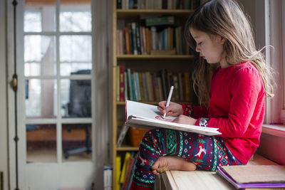 Side view of a little girl drawing pictures in her pajamas by window