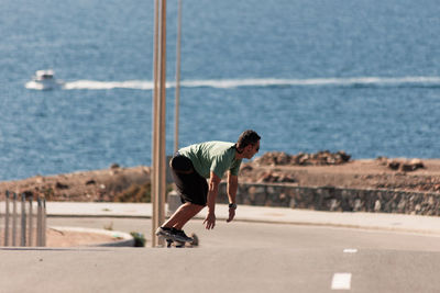 A man playing figure skating on a rural road in the sun on a bright day, play surf skate near coast