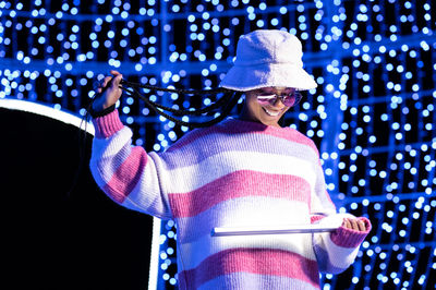 Joyful woman of color with a white beanie braided hairstyle and pink glasses enjoying the christmas