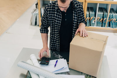 High angle view of salesman using calculator by cardboard box in store