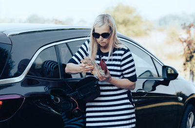 Portrait of young woman standing against car