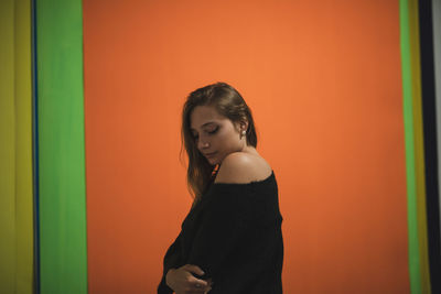 Young woman standing against orange wall