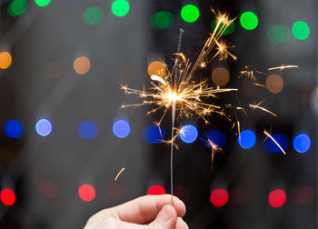 Close-up of person holding sparkler against illuminated background