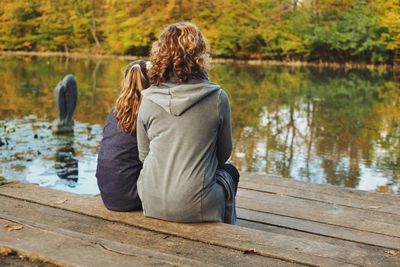 Rear view of woman sitting on jetty overlooking lake