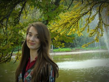 Portrait of smiling young woman standing by pond in garden