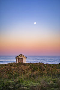 Wooden hut at scenic beach against sky during sunset