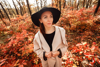 Woman wearing hat looking away amidst autumn forest