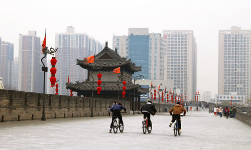 People riding bicycle on modern buildings in city against sky