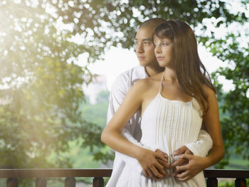 Young man embracing girlfriend while standing by railing in balcony