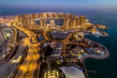 Illuminated cityscape by sea against sky during sunset