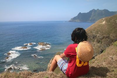 Rear view of woman with asian style conical hat looking at sea against sky