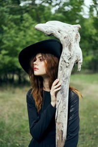 Portrait of young woman standing by tree trunk