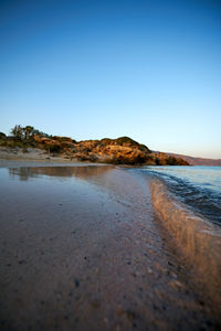 Surface level of beach against clear blue sky