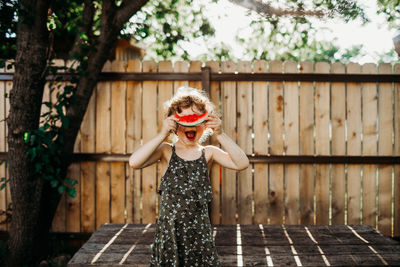 Young girl smiling and hiding behind slice of watermelon in spring