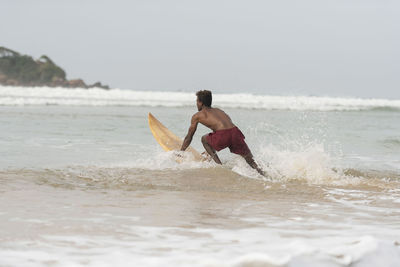 Shirtless man surfing in sea against sky