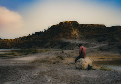 Rear view of man sitting on rock against sky