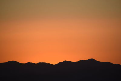 Scenic view of silhouette mountains against orange sky