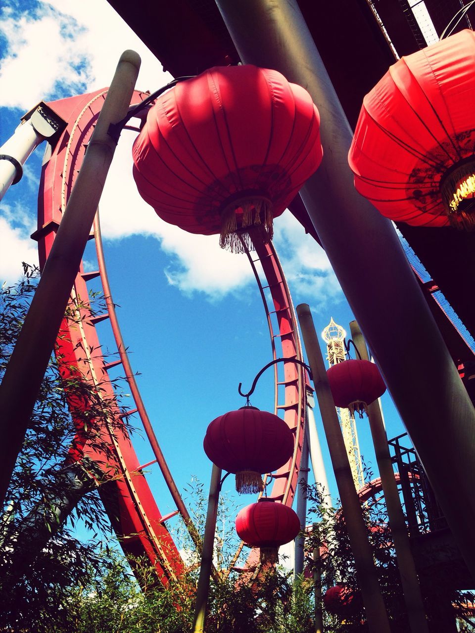 low angle view, sky, hanging, amusement park, amusement park ride, tree, lighting equipment, arts culture and entertainment, lantern, decoration, illuminated, celebration, ferris wheel, cloud - sky, built structure, fun, dusk, outdoors, architecture, balloon