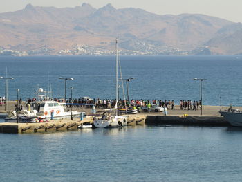 People on pier at port on sea against mountains