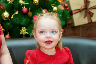 A beautiful little girl with bright blue eyes on the background of a christmas tree looks away 