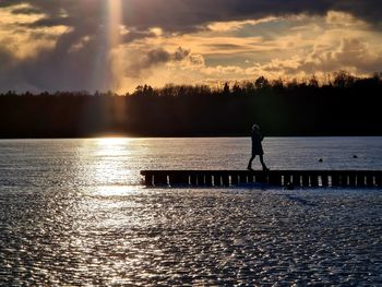 Silhouette man standing by lake against sky during sunset