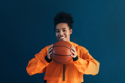 Young woman playing basketball while standing against blue background