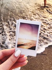 Close-up of woman hand holding photographs at beach