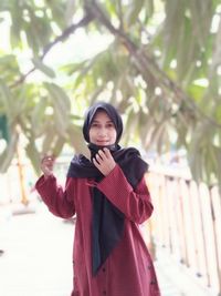 Portrait of smiling young woman standing against tree