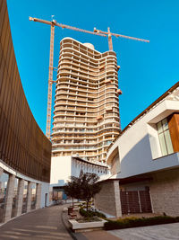 Crane working on construction site, building  a modern monolitic skyscraper against turquoise sky