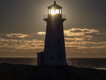 Lighthouse by sea against sky during sunset