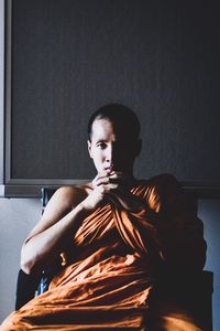 Portrait of young woman sitting against wall