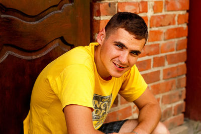 Portrait of young man standing against brick wall