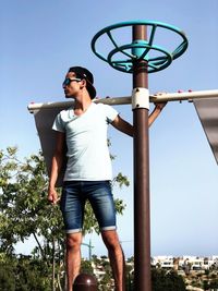 Low angle view of man standing by pole against clear sky