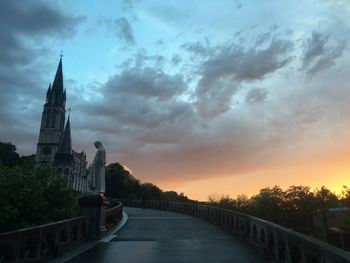 Narrow walkway leading to church against cloudy sky