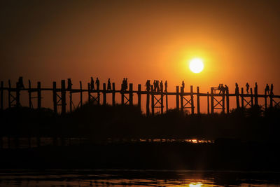 Silhouette bridge over river against sky during sunset