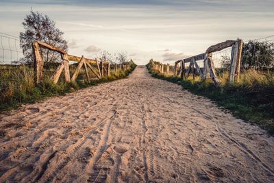 Dirt road amidst field against sky