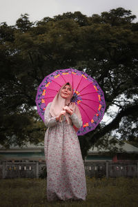 Woman with pink umbrella standing against trees